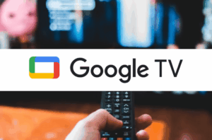 A wide, white horizontal banner is centrally placed over a blurred image. The blurred background shows a hand holding a black remote control in the lower portion, pointed towards a brightly illuminated television screen in the upper portion, which displays abstract, colorful content.

The white banner prominently features the Google TV logo. On the left, there's a stylized icon resembling a television screen, composed of a blue rectangle with a red left edge, a green top edge, and a yellow bottom edge.