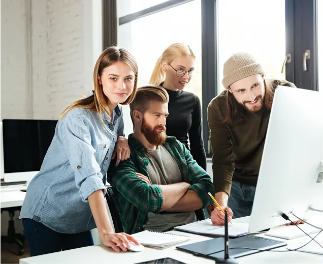 A diverse group of people gathered around a computer screen, engaged in discussion and observation.